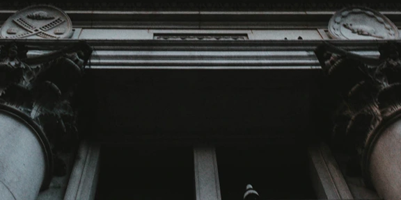 Dark, low-angle view of a classical building facade with ornate columns and decorative circular reliefs.