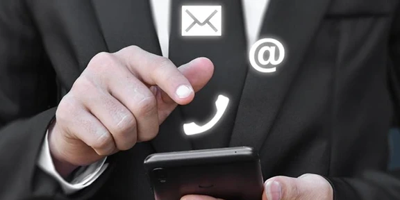 Person in suit using smartphone with floating email, phone, and at symbols.