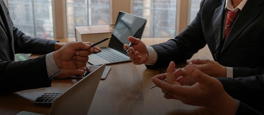 Business professionals in suits engaged in a discussion around a wooden table with laptops.
