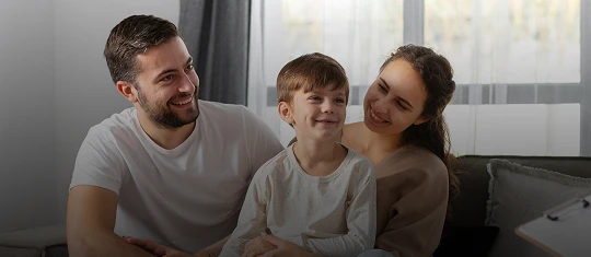 Smiling family of three sitting together in a bright living room with neutral tones.