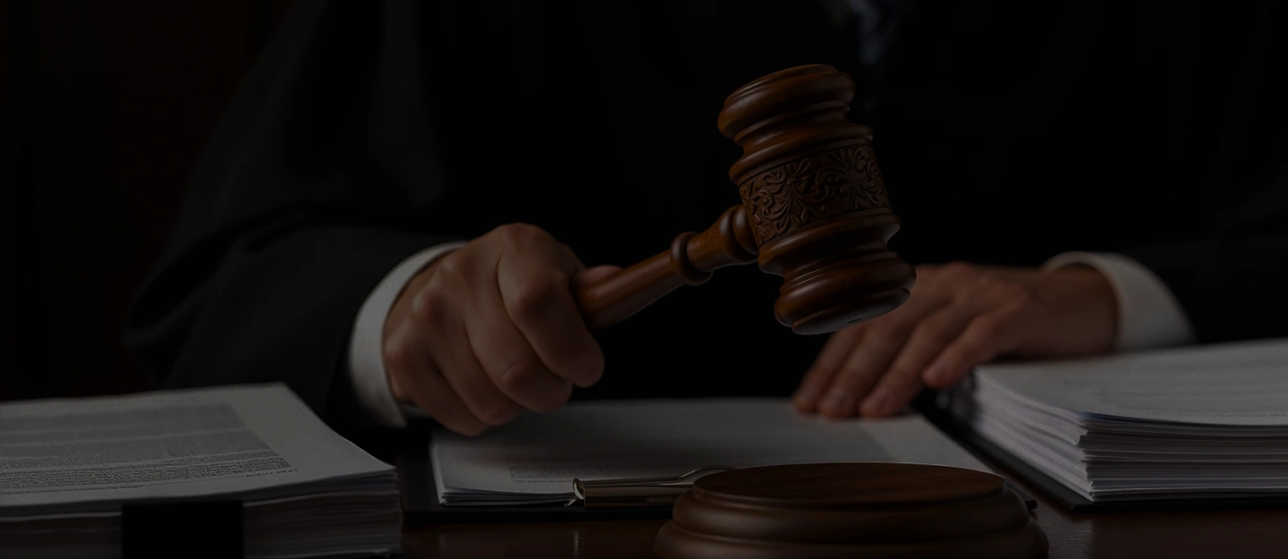 Judge in black robe holding wooden gavel over legal documents on desk.