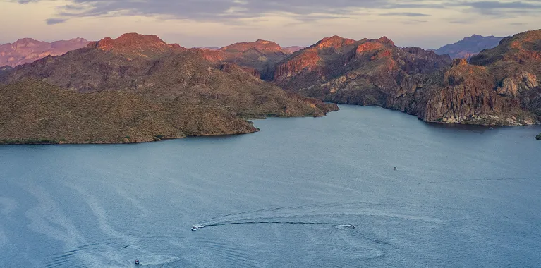 Aerial view of a large blue lake surrounded by rugged brown mountains during sunset.