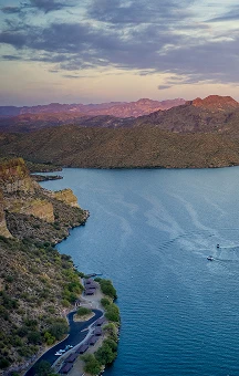 Aerial view of a blue lake surrounded by rocky hills under a cloudy sky at sunset.