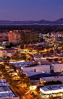 Aerial nighttime view of a cityscape with illuminated buildings and distant mountains.