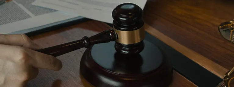 Wooden judge's gavel resting on sound block on a dark wooden desk.