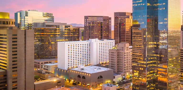 Downtown cityscape at sunset with modern glass skyscrapers and illuminated buildings.