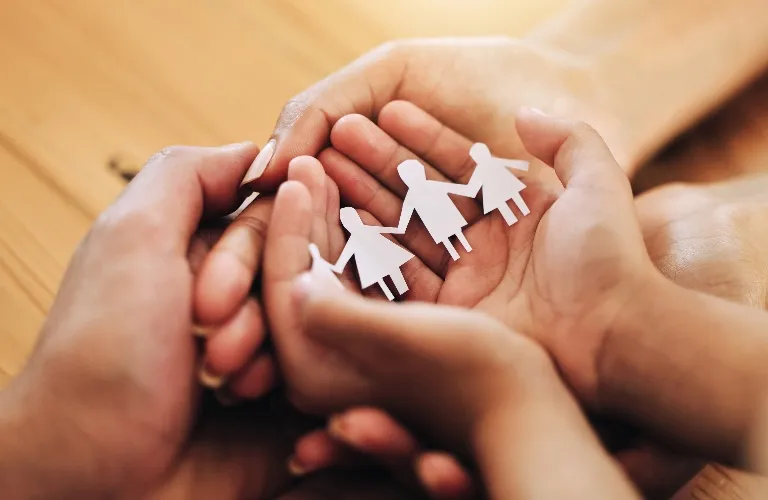 Close-up of adult and child hands holding paper cutouts of a family on wooden surface.