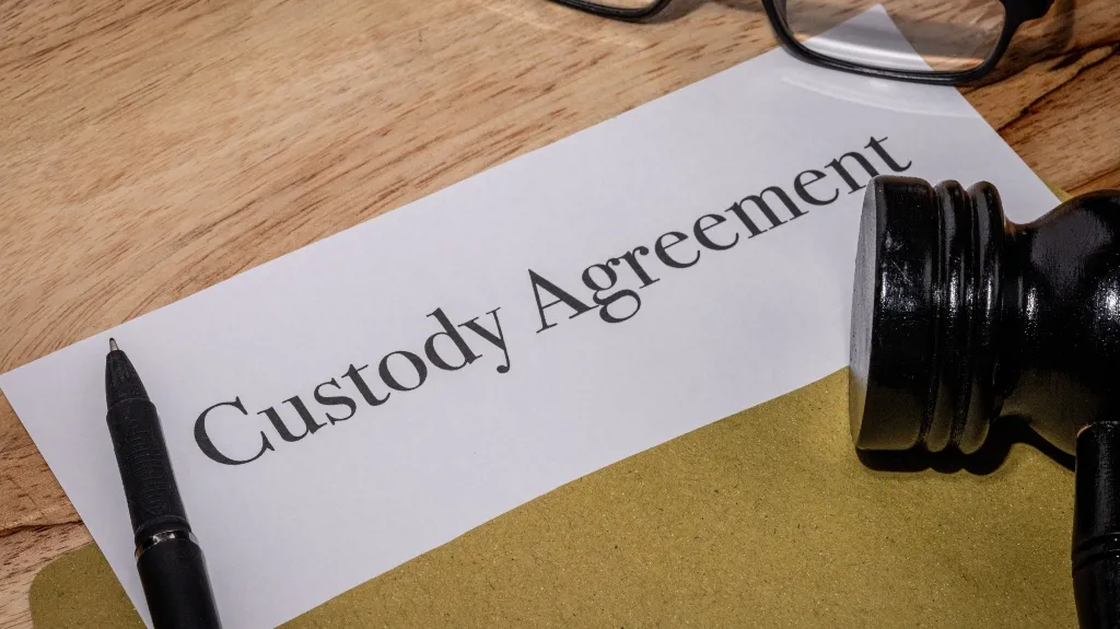 Document titled "Custody Agreement" on wooden surface with black pen, judge's gavel, and eyeglasses.
