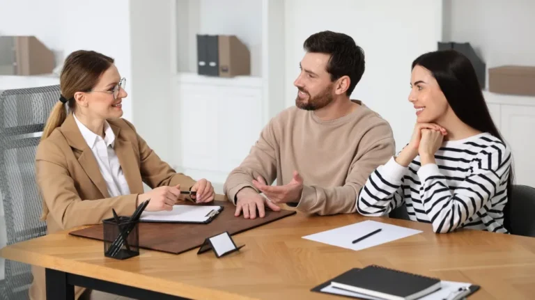 Three professionals engaged in a discussion at a wooden office desk with documents and stationery.