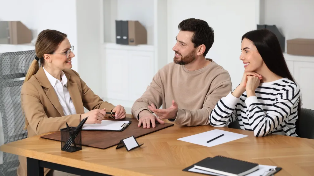 Three professionals engaged in a discussion at a wooden office desk with documents and stationery.