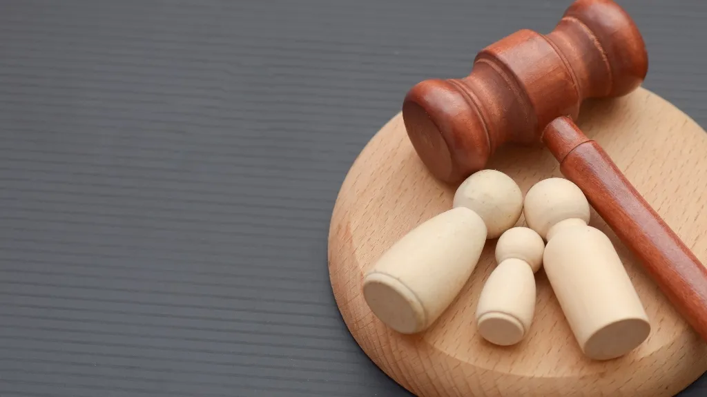 Wooden judge's gavel and base with three beige wooden figurines on a gray surface.