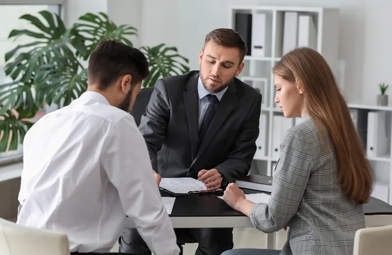Three professionals in business attire engaged in discussion over documents at a modern office desk.