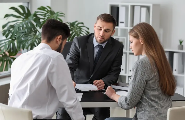Three professionals engaged in a discussion around a table in a modern office setting.