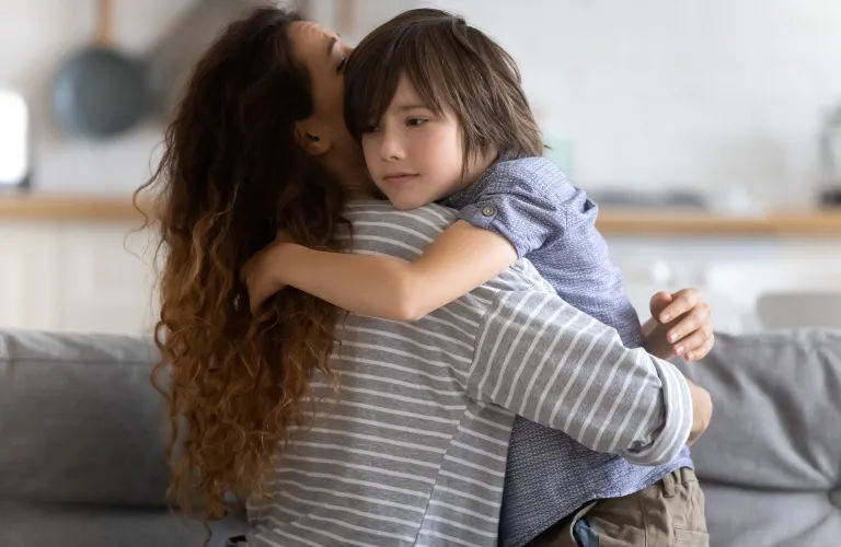 Woman with long curly hair in a striped shirt embracing a young boy in a blue shirt.