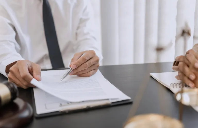Two professionals at a desk reviewing documents, with a gavel and scales of justice nearby.