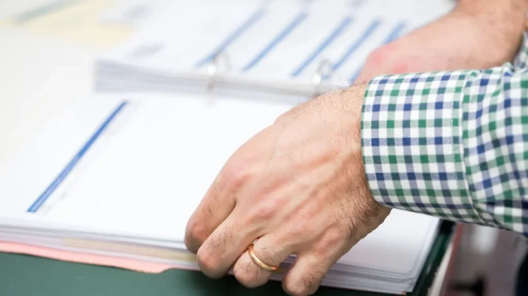 Close-up of a person’s hand with a gold ring flipping through a binder with printed documents.