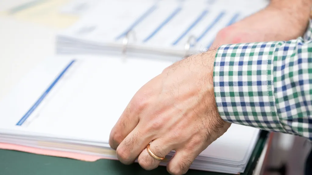 Close-up of a person’s hand with a gold ring flipping through a binder with printed documents.