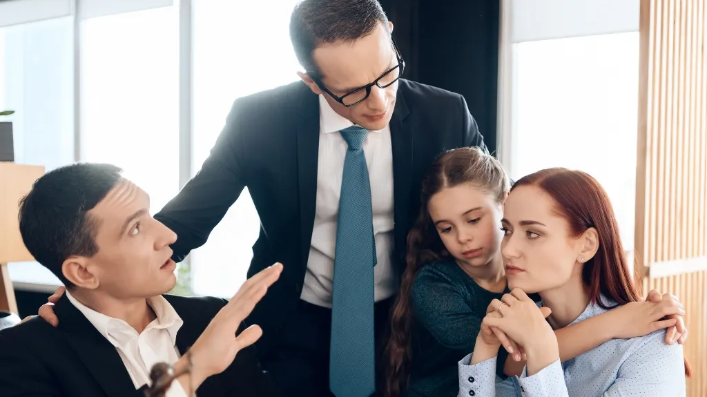 Four people in a professional setting, with a man in a suit comforting a woman and child.