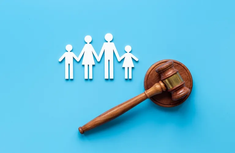 Wooden judge's gavel beside white paper cutout figures of a family on blue background.