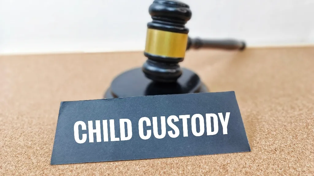Black judge's gavel and nameplate with white text reading "CHILD CUSTODY" on cork surface.